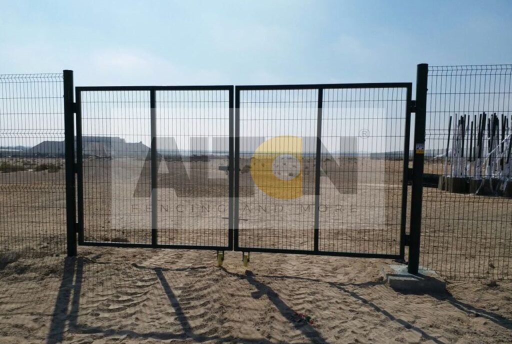 Construction site with large, grey concrete blocks placed at regular intervals, supporting a tall metal fence.